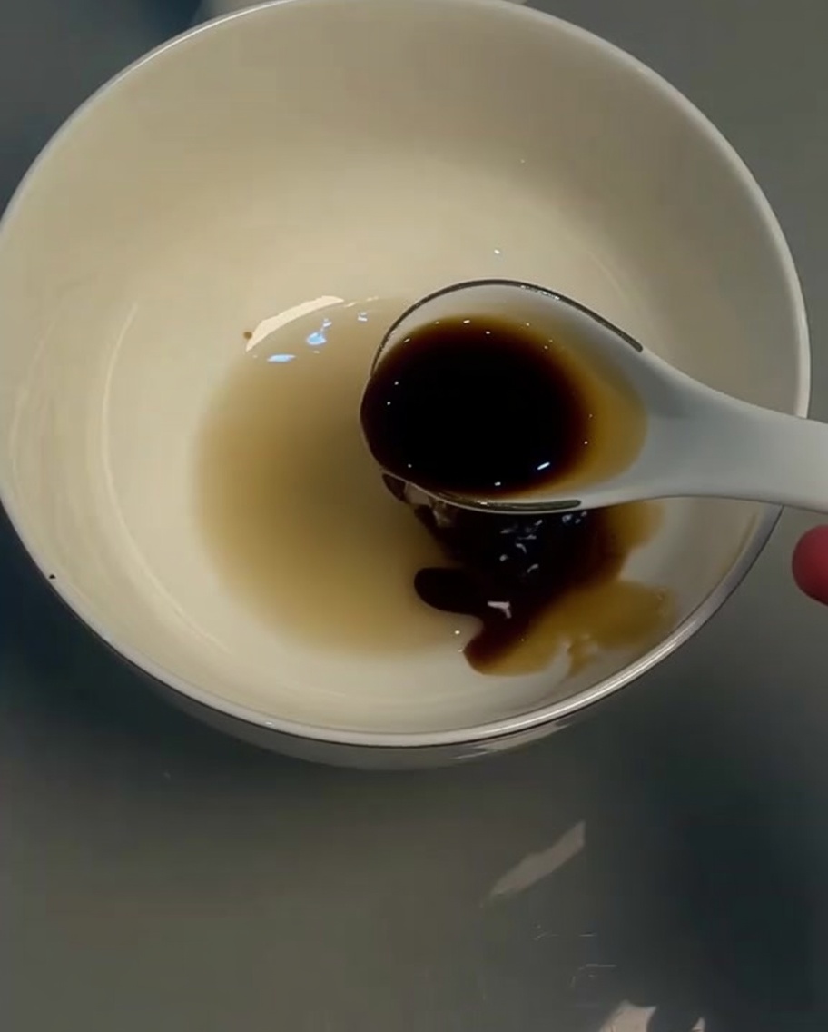 Salsa de soja ligera en un bol blanco siendo removida con una cuchara.
