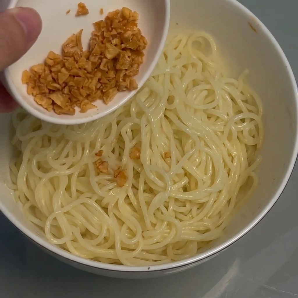 Ajo frito crujiente siendo espolvoreado sobre un bol de fideos.