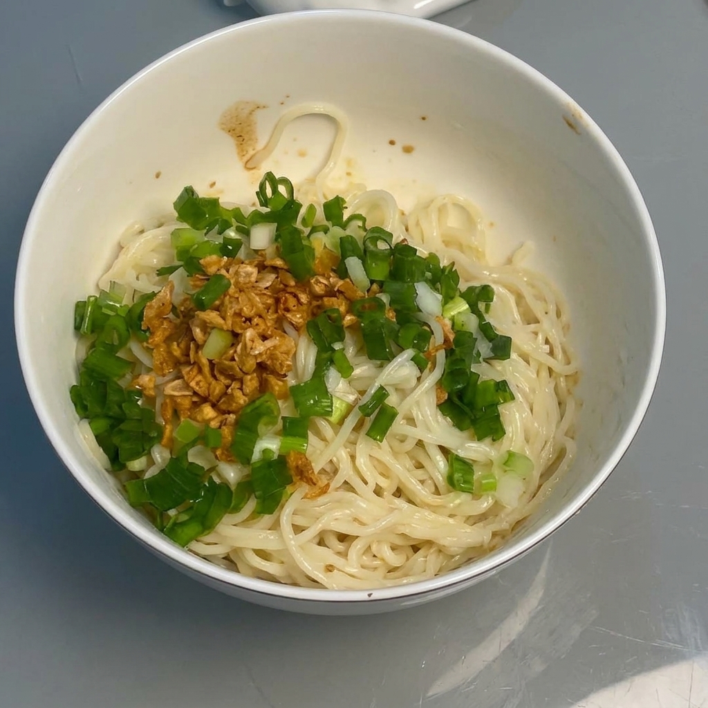 Fideos mezclándose con la salsa, el ajo y las cebolletas usando unos palillos.
