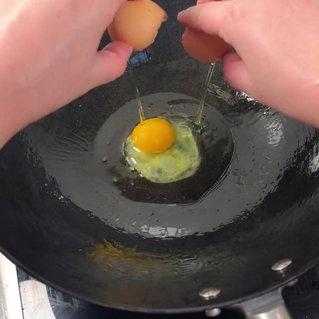 Dos huevos friéndose en un wok caliente con aceite, mostrando bordes crujientes.