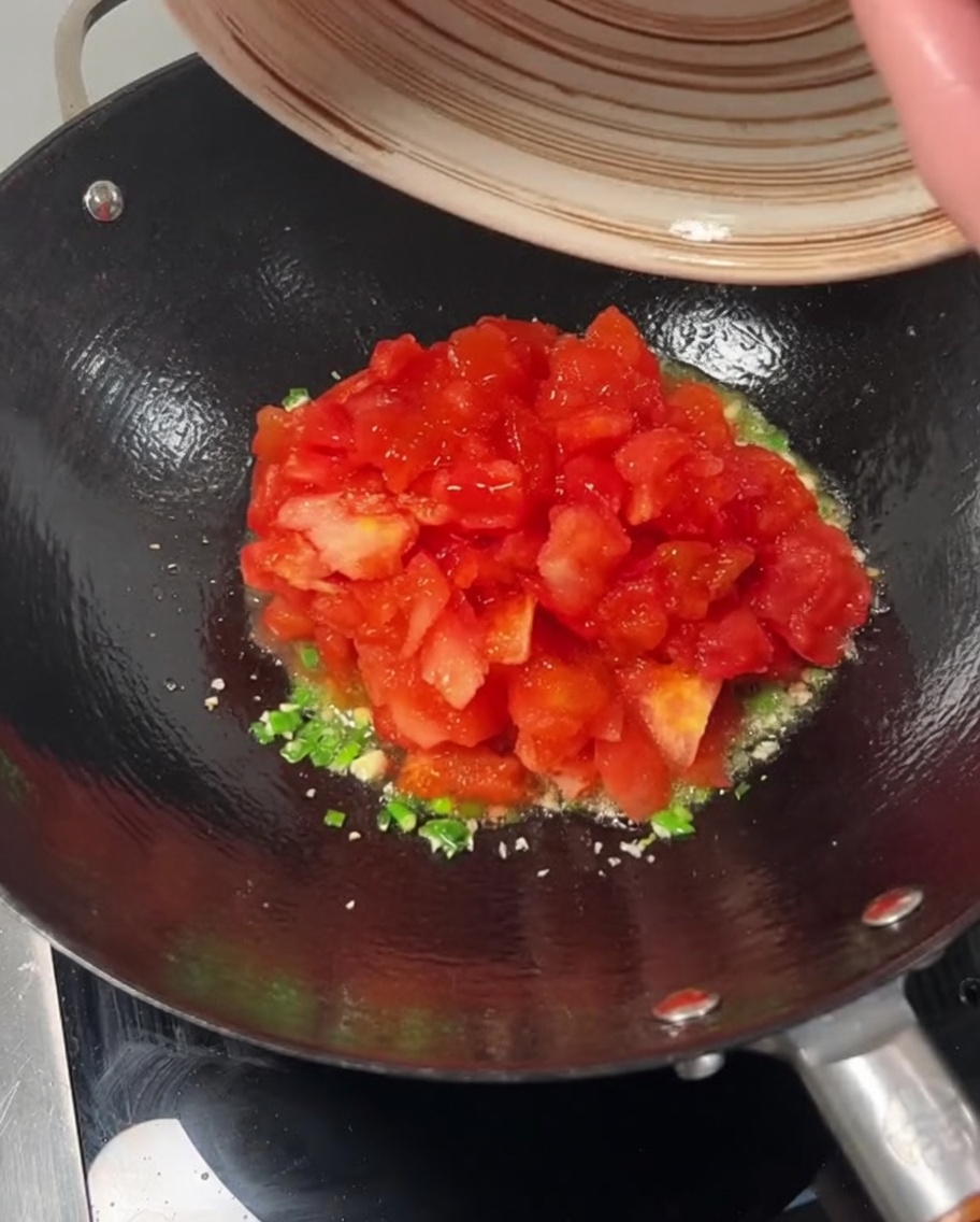 Tomates cortados en dados vertiéndose en un wok con ajo y cebolleta.