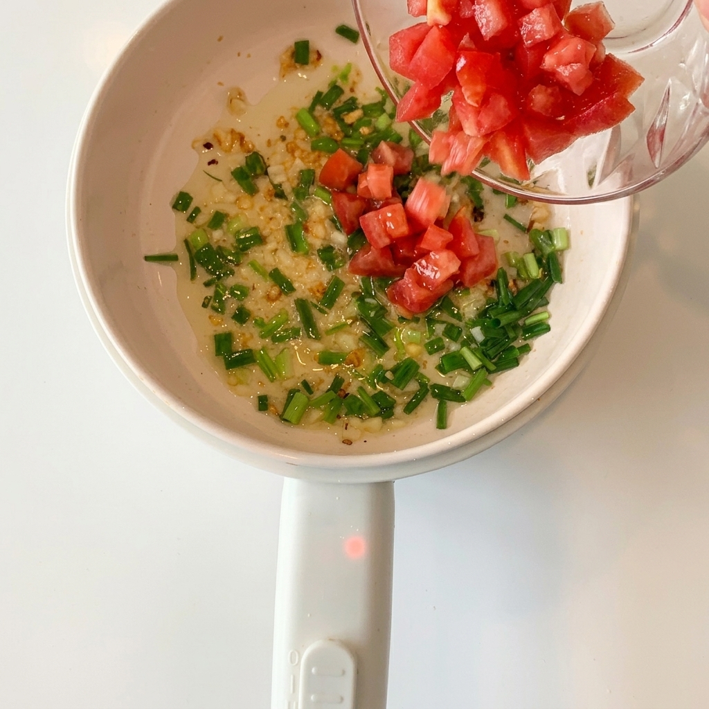 Tomates rojos cortados en cubitos añadidos a la olla que contiene el ajo y las cebolletas salteadas.