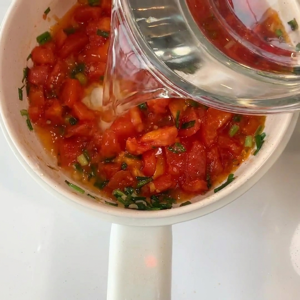 Agua limpia siendo vertida desde un bol de cristal a la olla con los tomates.
