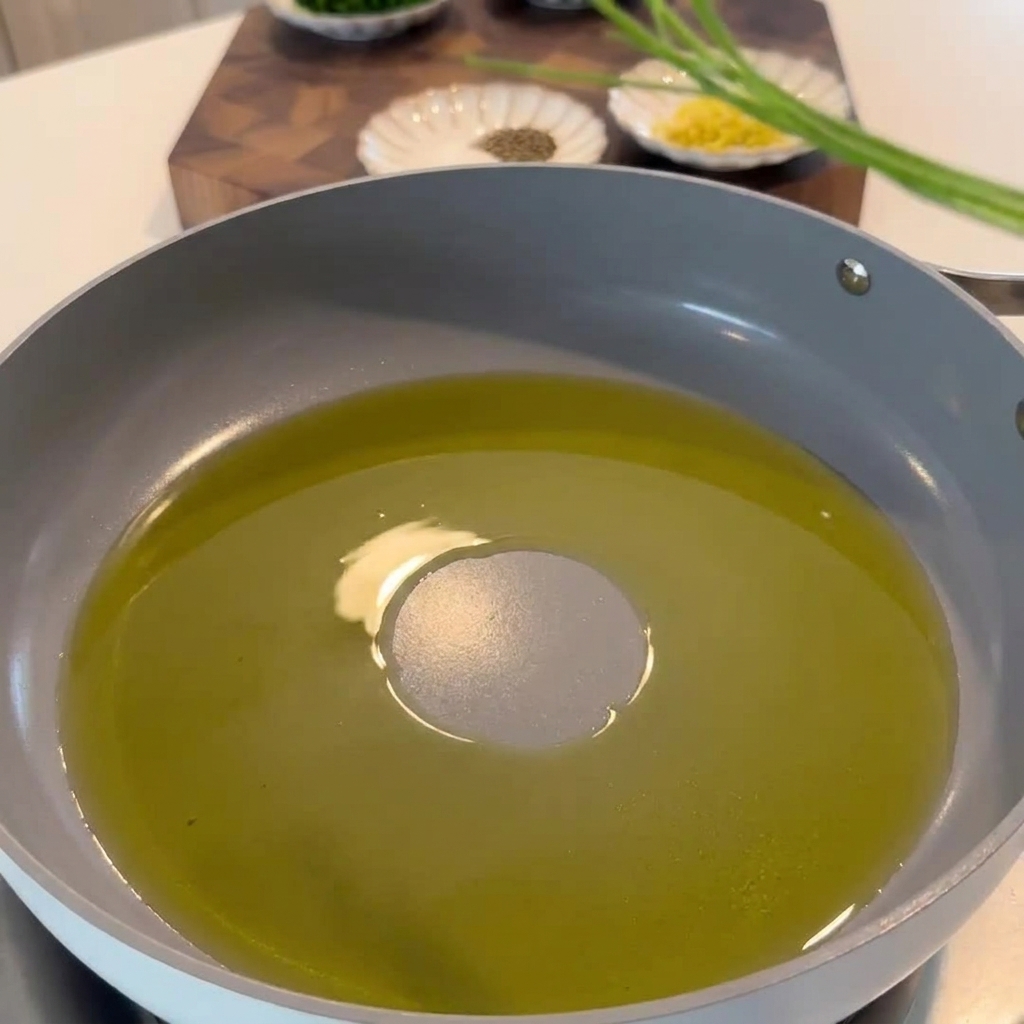 Tallos de perejil, ralladura de limón y copos de chile siendo salteados en una sartén con aceite de oliva aromatizado con ajo.
