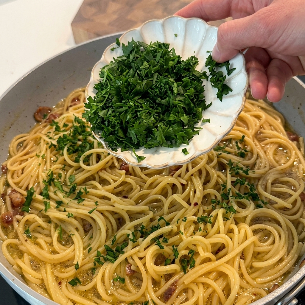 Perejil fresco picado siendo espolvoreado sobre la pasta terminada en la sartén.