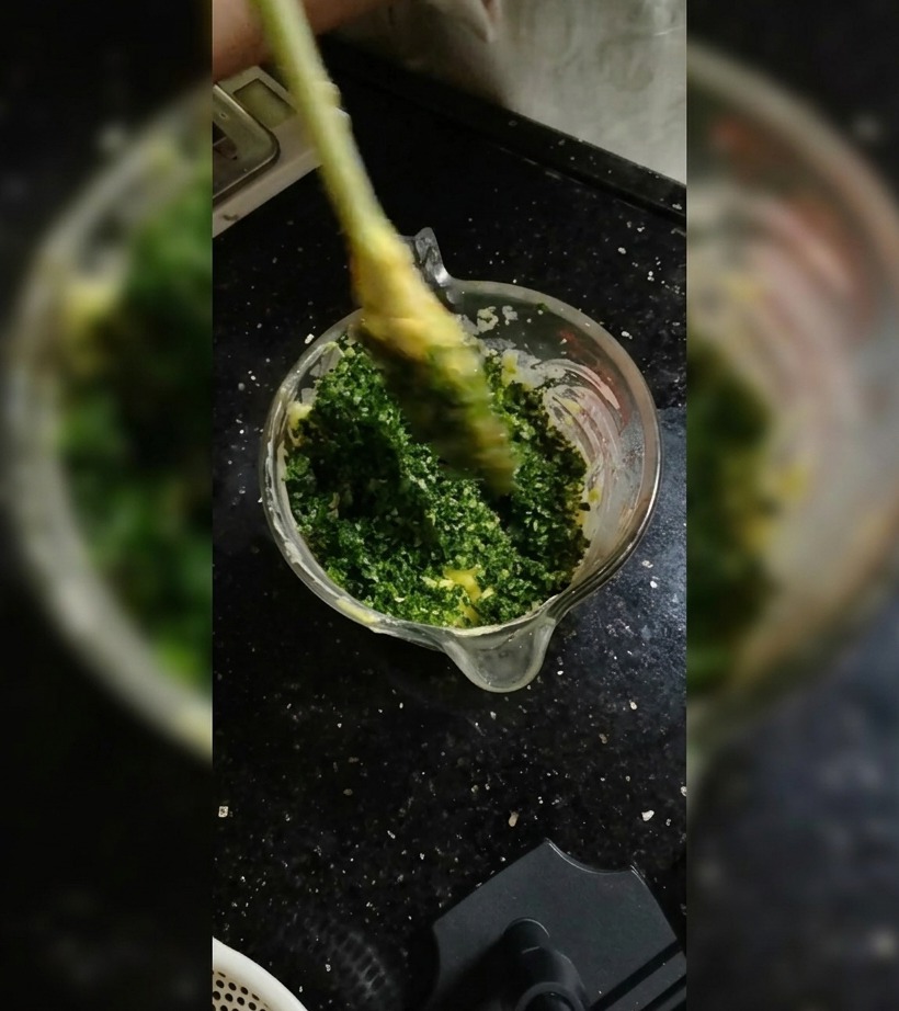 Una espátula de silicona incorporando las hierbas en la mantequilla blanda dentro de un bol de vidrio.