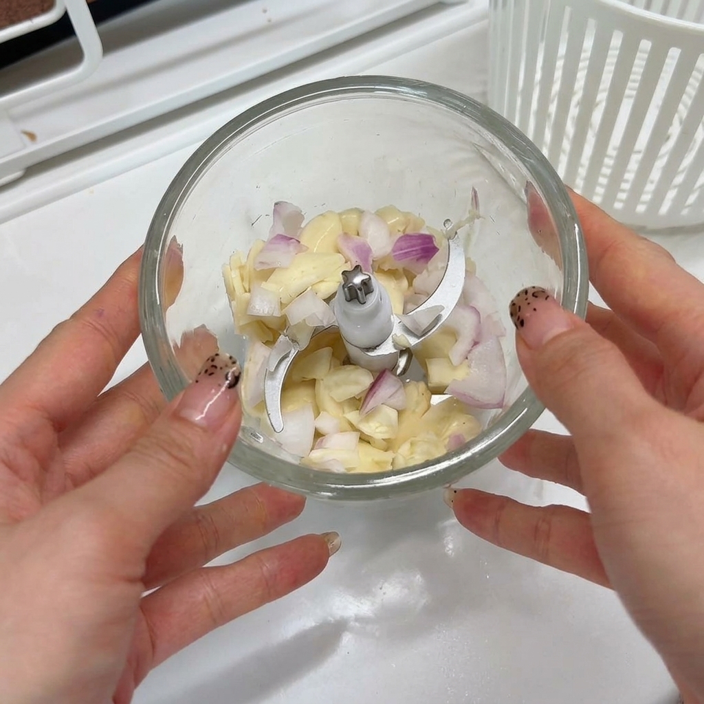 Dientes de ajo y chalotas picadas dentro del vaso de un pequeño procesador de alimentos, listos para ser triturados.
