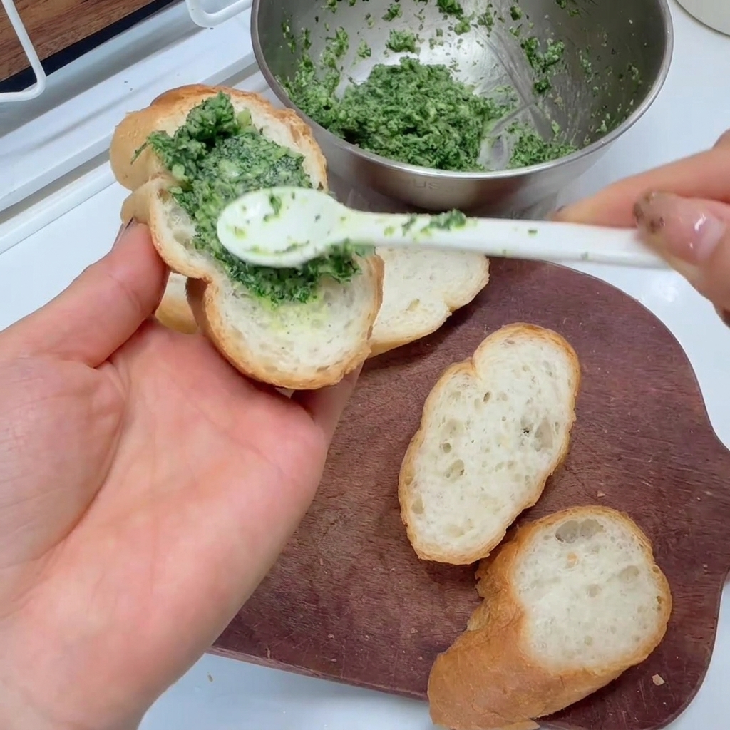 Untando una mezcla de un verde brillante de ajo y perejil sobre rebanadas de baguette con una cuchara.