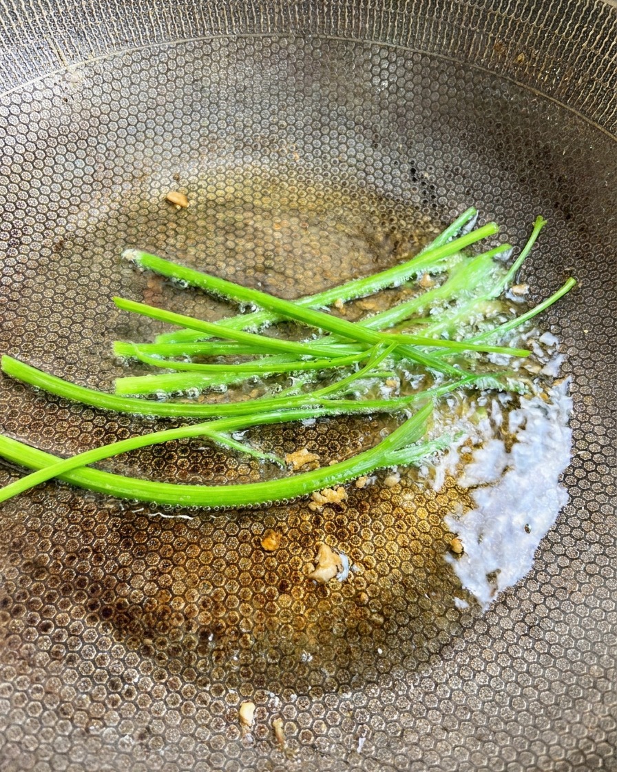 Tallos de perejil fresco verde siendo añadidos al aceite aromatizado con ajo en el wok.