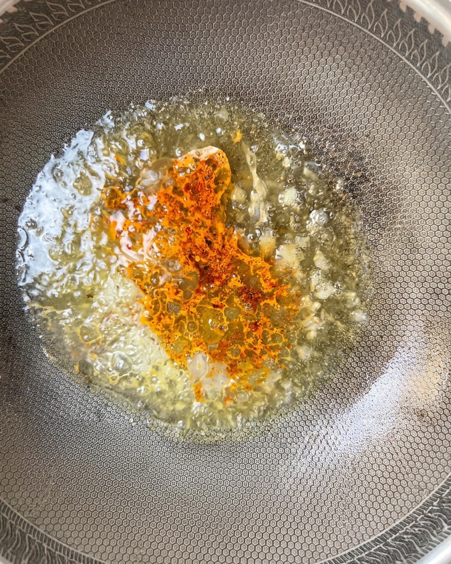 Chile en polvo siendo espolvoreado en la mezcla burbujeante dentro del wok.