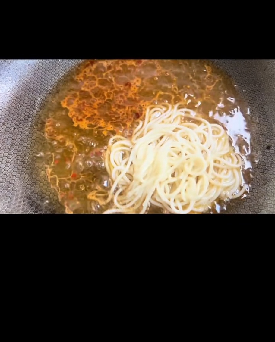 Espaguetis hervidos siendo transferidos al wok para mezclarlos con la salsa.
