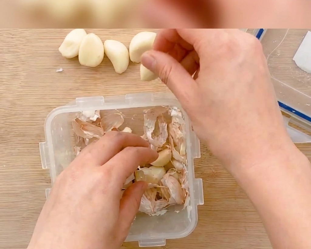 Dientes de ajo pelados siendo cortados en láminas finas sobre una tabla de madera.
