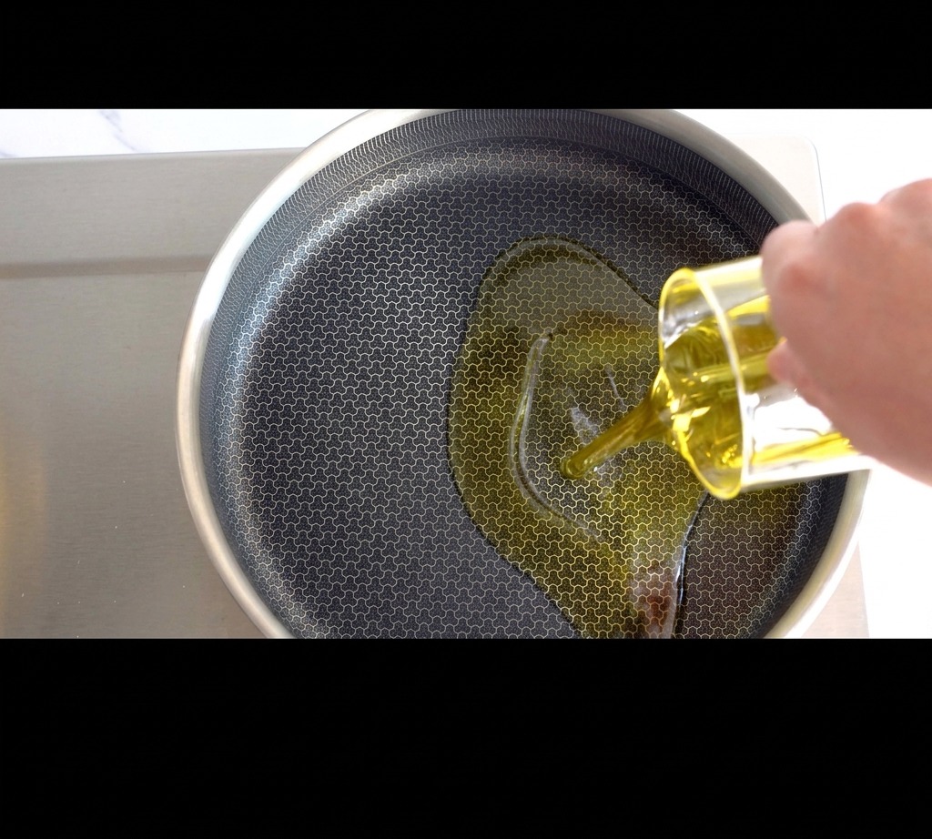 Aceite de oliva dorado vertiéndose en una sartén sobre la estufa.