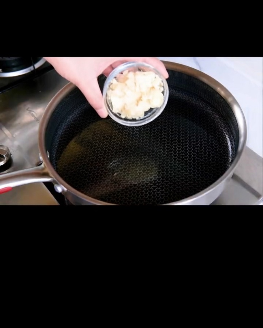 Ajo laminado friéndose en aceite de oliva brillante en una sartén.