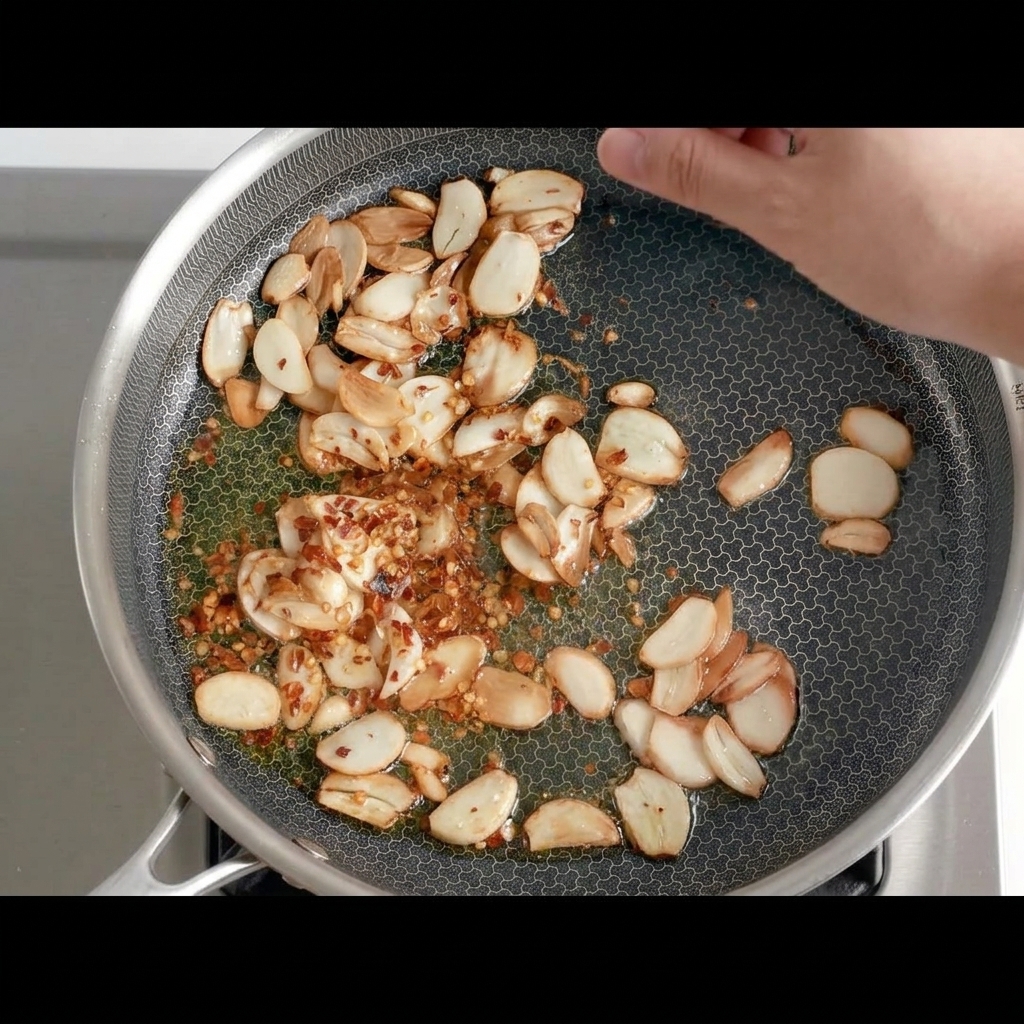 Trozos de chile seco siendo añadidos a la sartén con el ajo frito dorado.