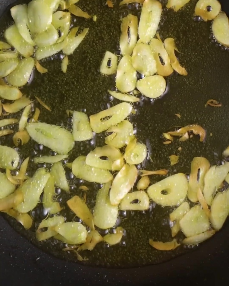 Láminas de ajo y chiles rojos vibrantes friéndose en aceite brillante dentro de una sartén.