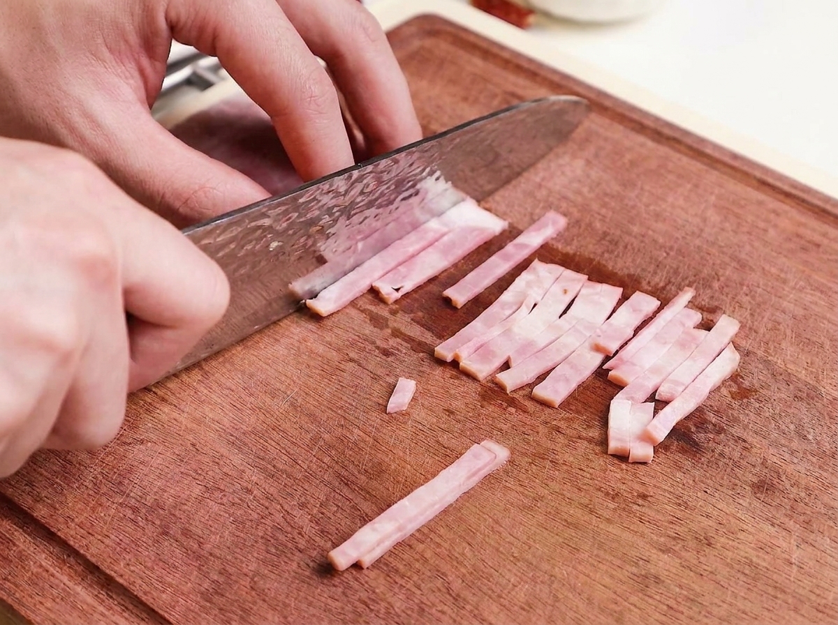 Tiras finas de bacon crudo siendo cortadas en una tabla de madera.