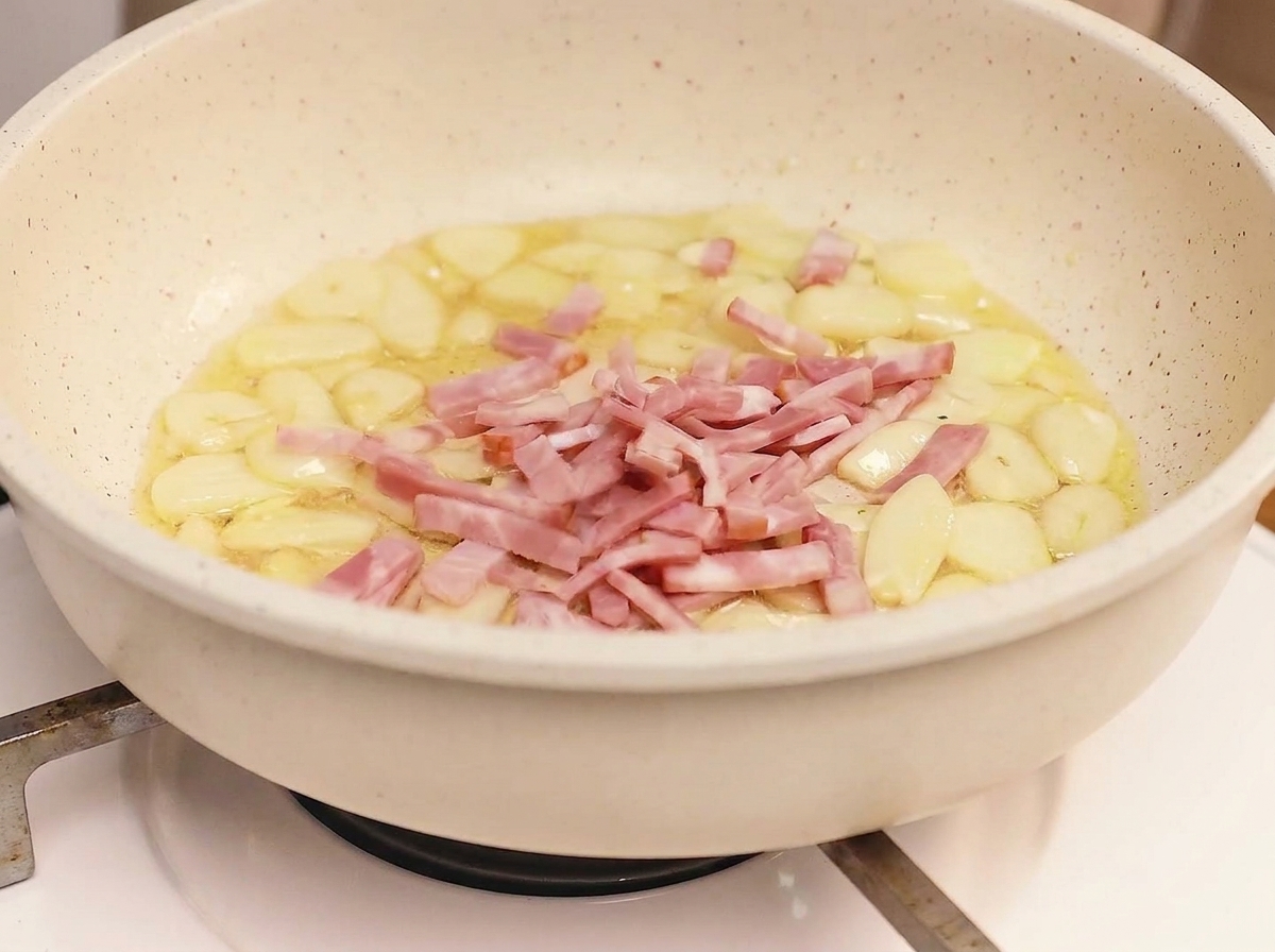 Tiras de bacon friéndose en una sartén con ajo, alcanzando un estado dorado, crujiente y marrón.