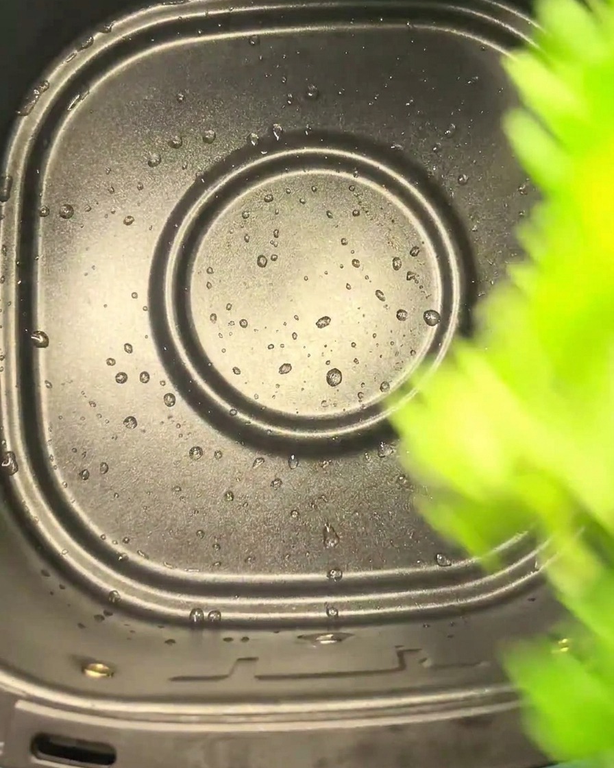 Hojas de apio verdes cayendo en la cesta negra de una freidora de aire.