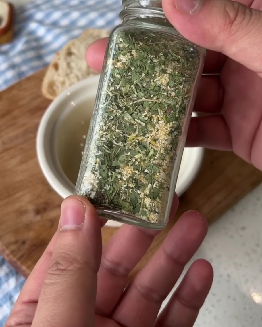 Un pequeño bol de cerámica con mantequilla ablandada, siendo sazonado con sal de ajo con perejil.