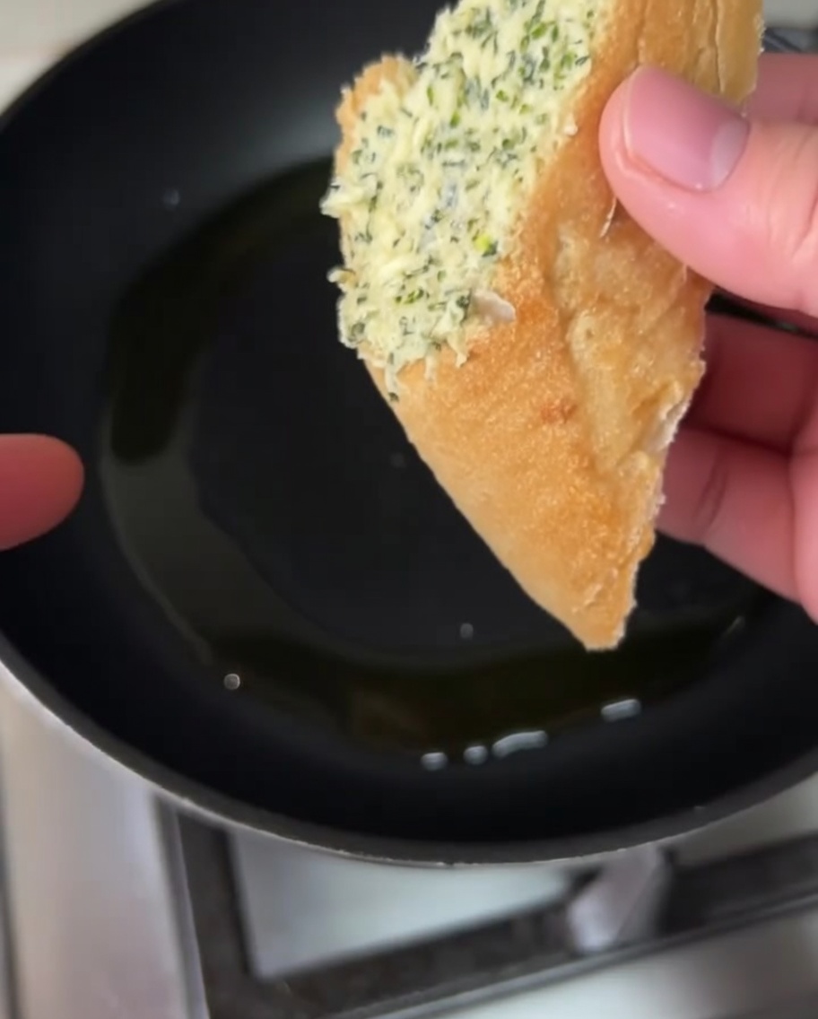 Rebanadas de pan cubiertas de mantequilla de ajo friéndose en una sartén con aceite de oliva.