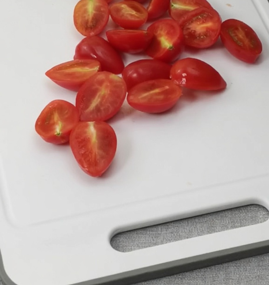 Tomates cherry cortados por la mitad sobre una tabla de cortar blanca.
