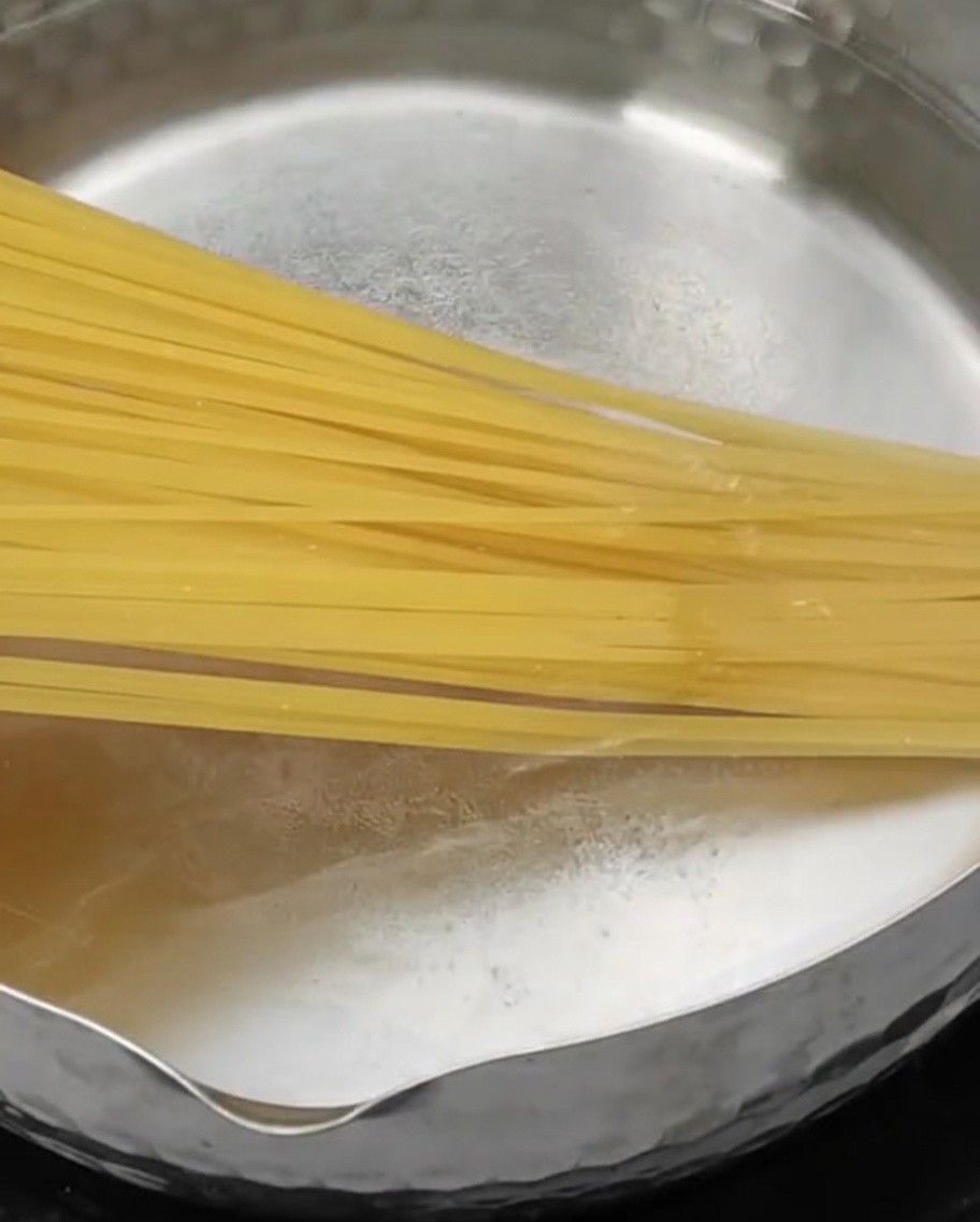 Pasta larga siendo introducida en una olla de acero inoxidable con agua hirviendo.