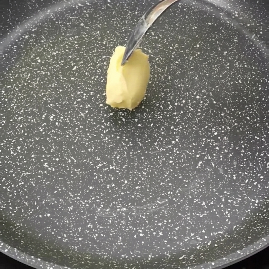 Una porción de mantequilla derritiéndose en una sartén antiadherente oscura.