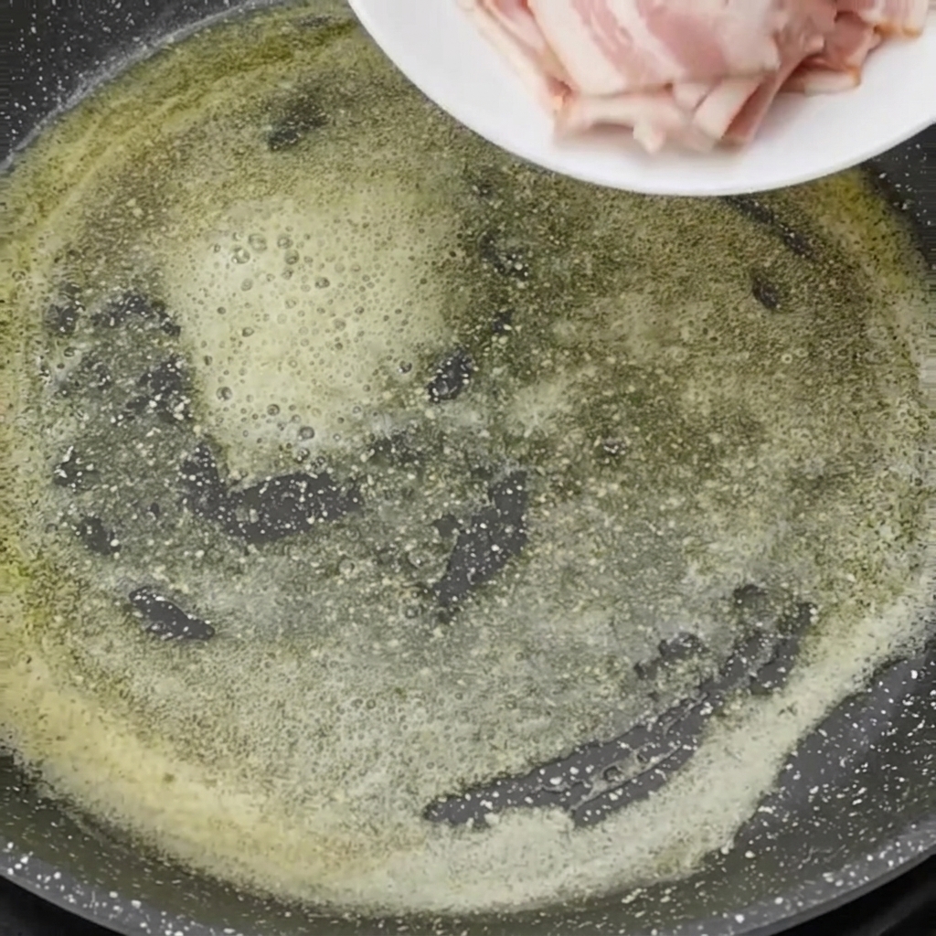 Trozos de bacon crudo siendo echados en una sartén con mantequilla derretida burbujeante.