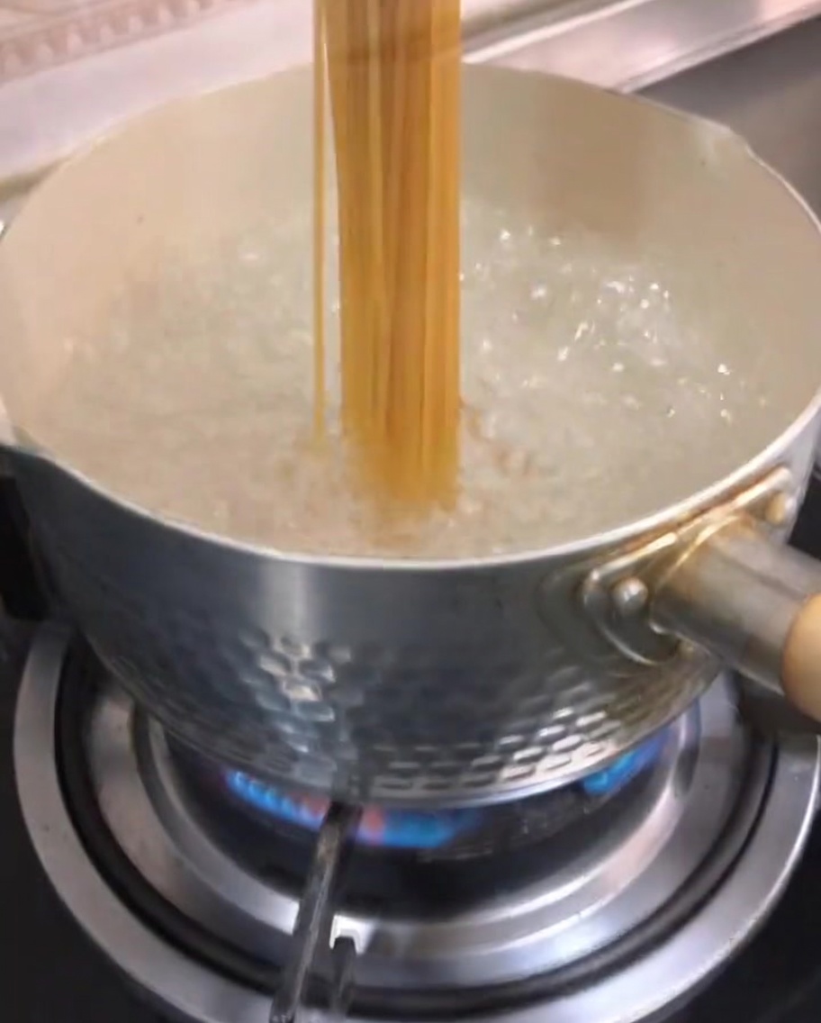 Espaguetis secos sumergiéndose en agua hirviendo.