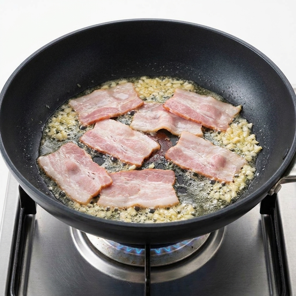 Trozos de bacon chisporroteando en la sartén junto al ajo dorado.