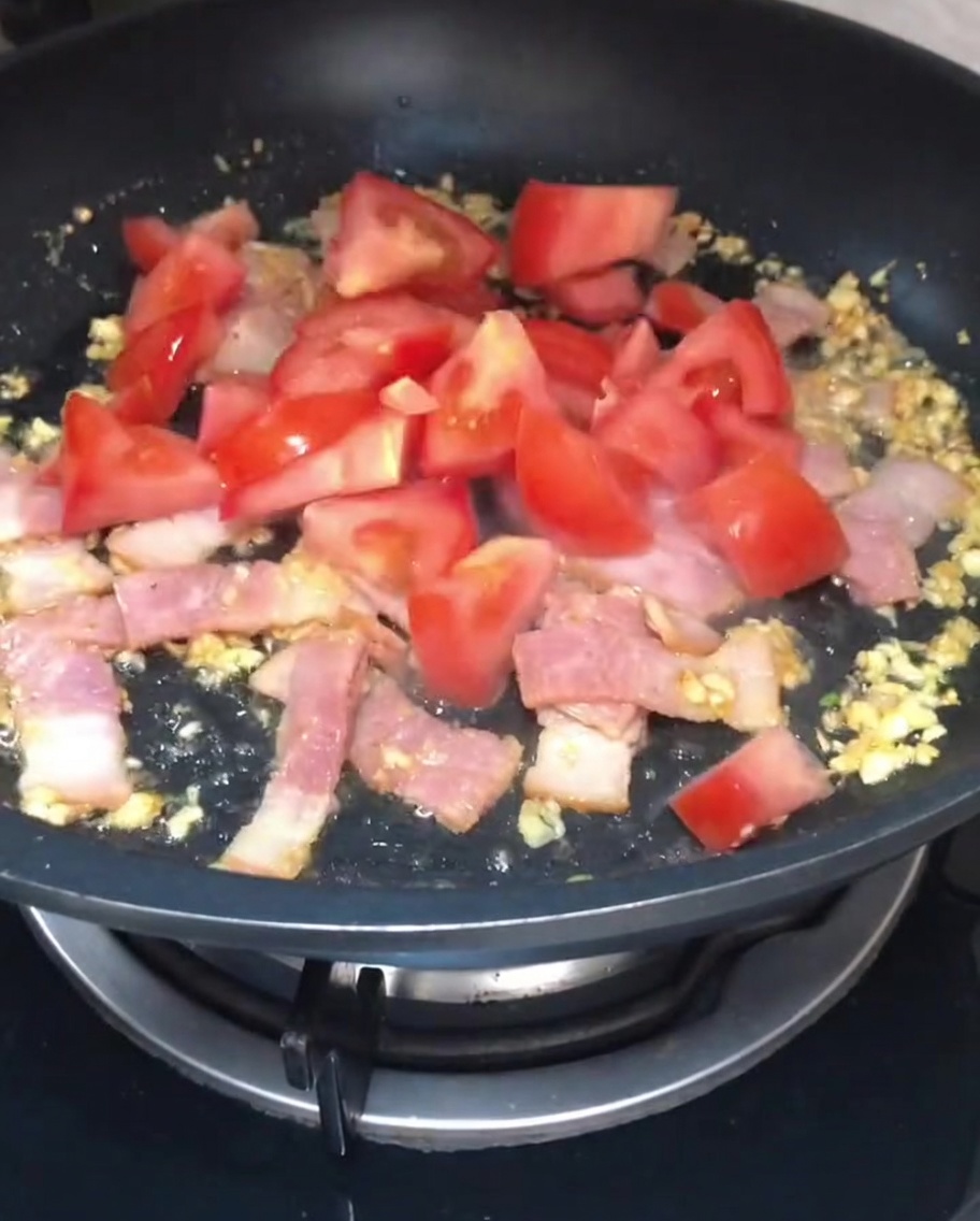 Trozos de tomate rojo añadidos al bacon y ajo en la sartén.