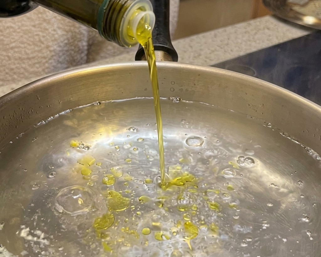 Vertiendo aceite de oliva en una olla con agua hirviendo.