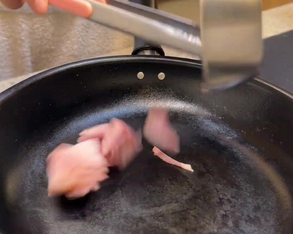 Añadiendo trozos de bacon a una sartén negra para freír.