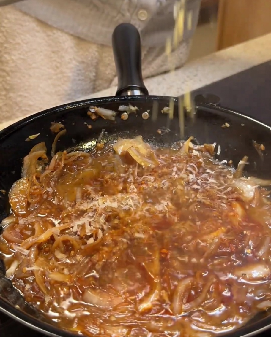 Queso parmesano siendo rallado sobre una salsa cremosa a fuego lento.