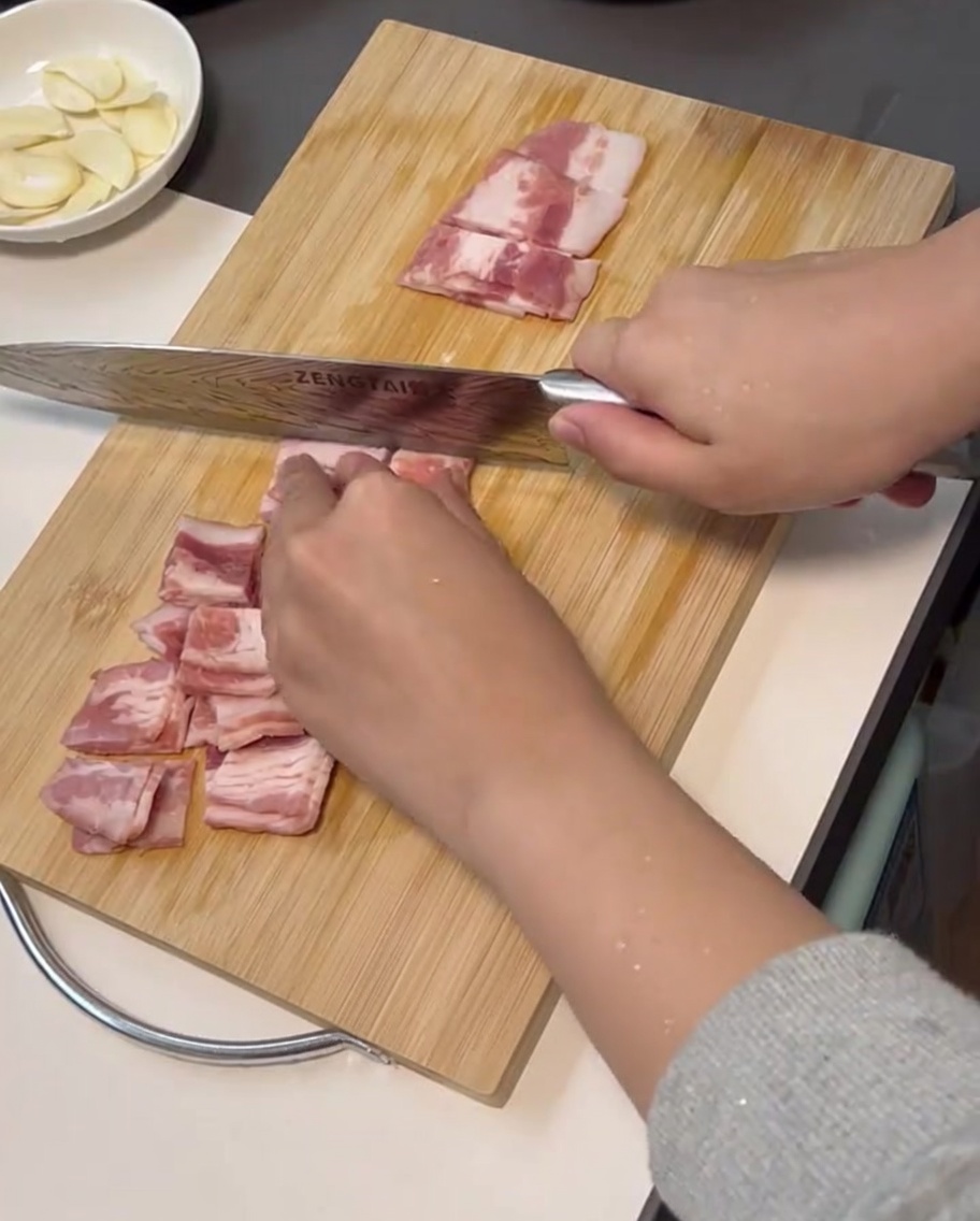 Tiras de bacon fresco siendo cortadas en trozos pequeños y uniformes.