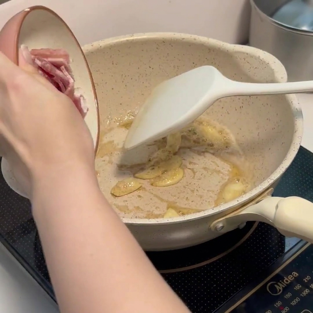 Trozos de bacon picado friéndose en la sartén junto al ajo aromático.