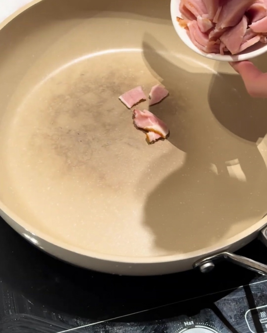 Trozos de bacon magro chisporroteando en una sartén seca, empezando a soltar su grasa.