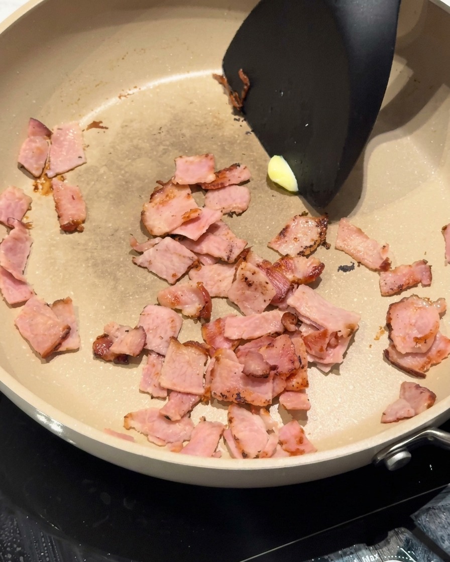 Una nuez de mantequilla amarilla derritiéndose en la sartén junto al bacon dorado.