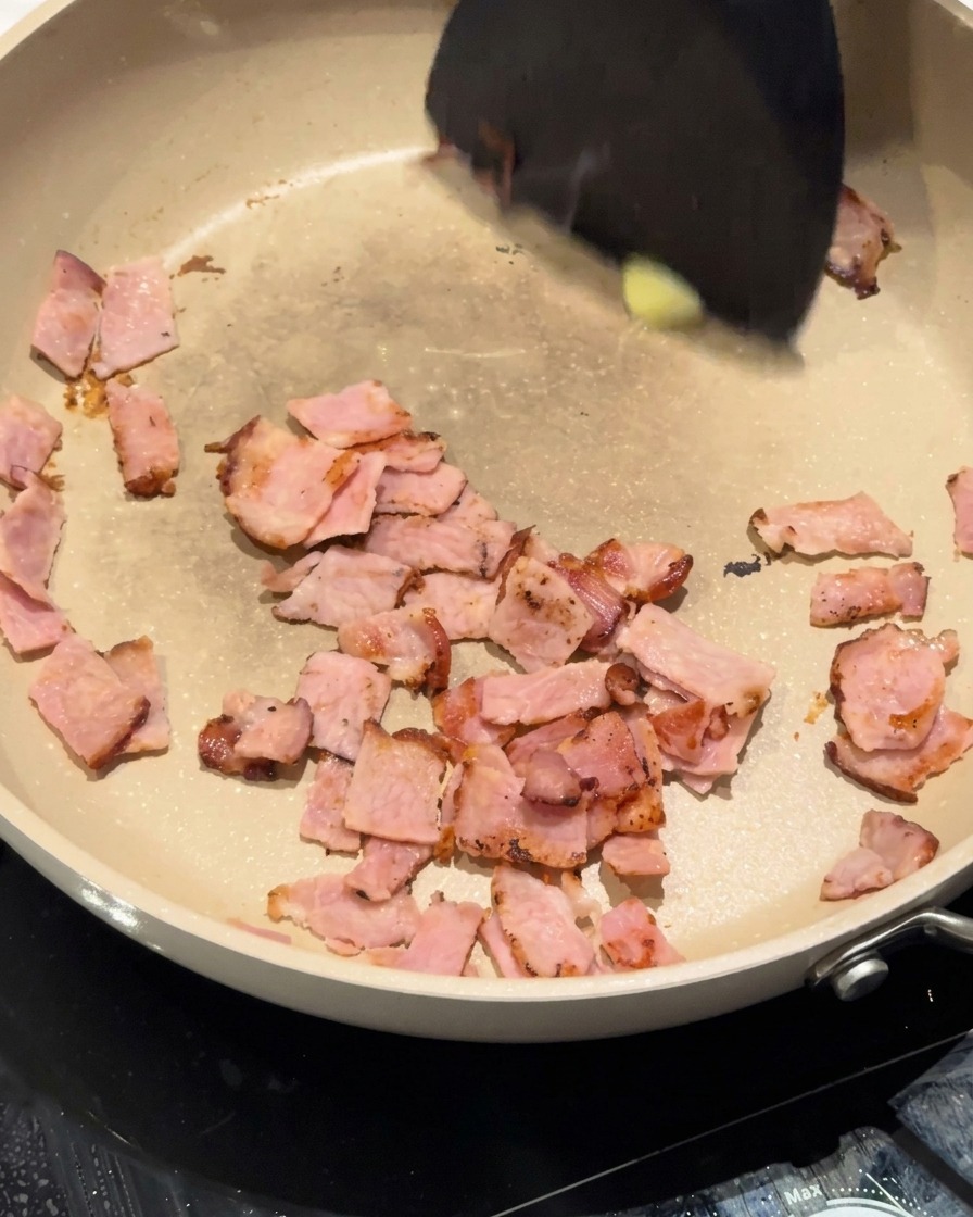 Cebolla blanca picada siendo removida en la sartén con el bacon y la mantequilla.