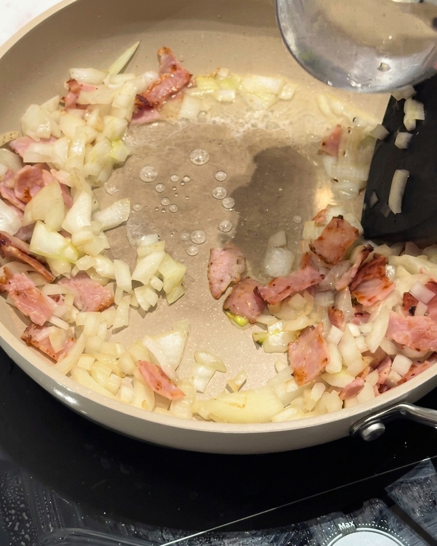 Fideos rizados siendo colocados en la sartén sobre la base de bacon y cebolla.