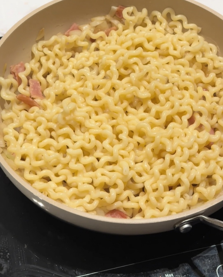 Leche baja en grasa siendo vertida sobre los fideos en la sartén.