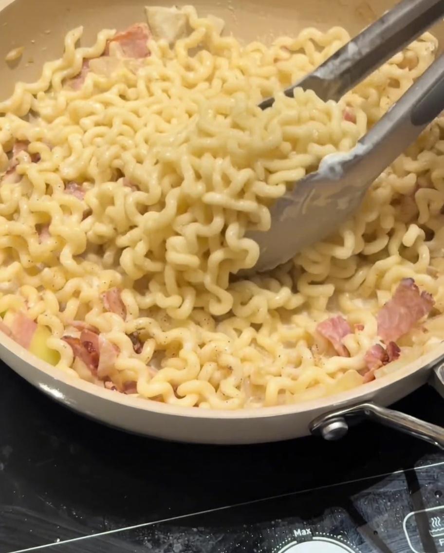 Queso parmesano siendo espolvoreado sobre una sartén de pasta carbonara cremosa.