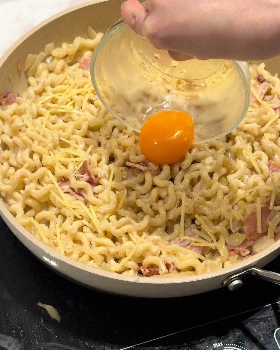 Una yema de huevo fresca siendo colocada cuidadosamente en el centro de un plato de pasta cremosa.