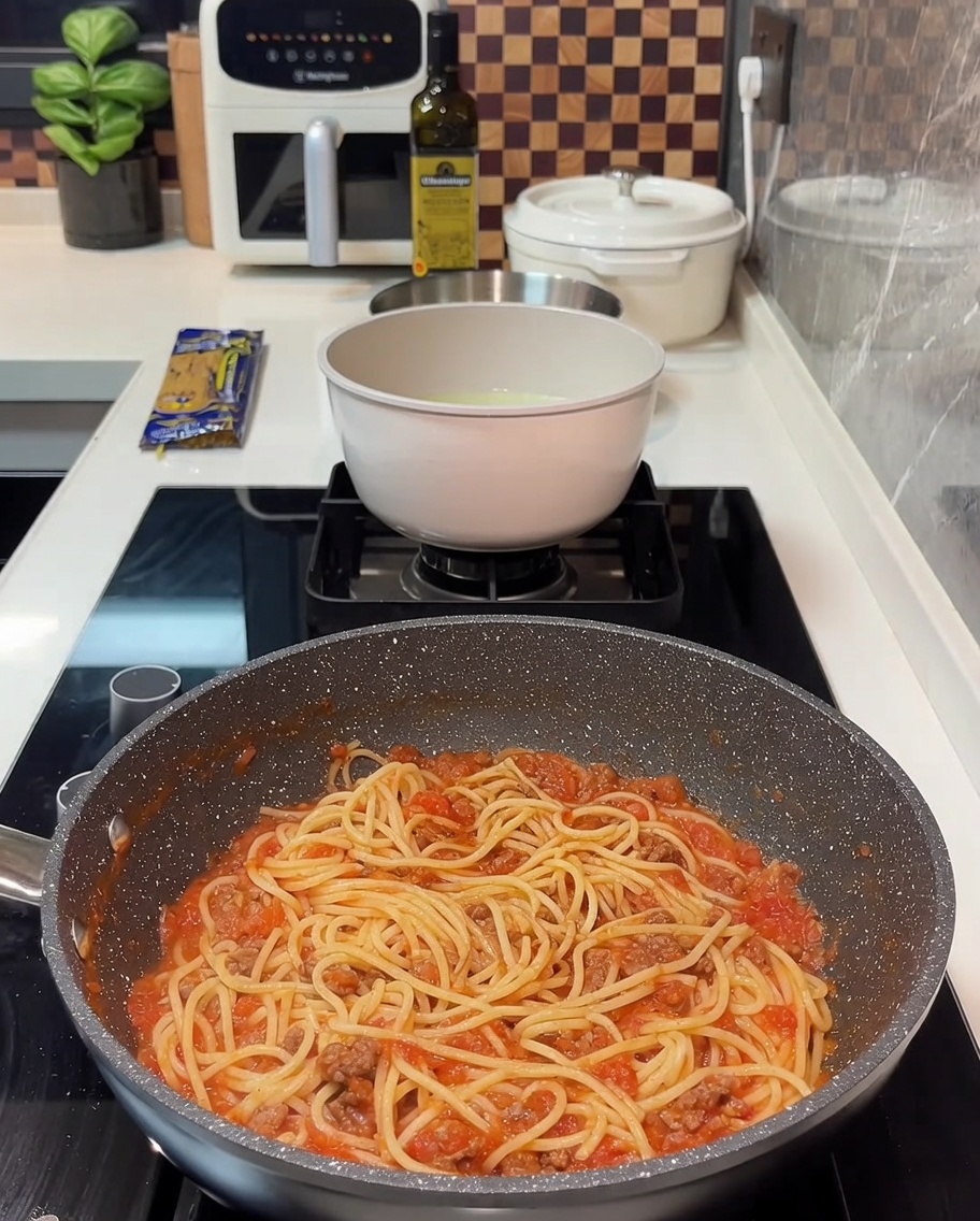 Sartén llena de espaguetis con salsa de carne y varias lonchas de queso derretido por encima.