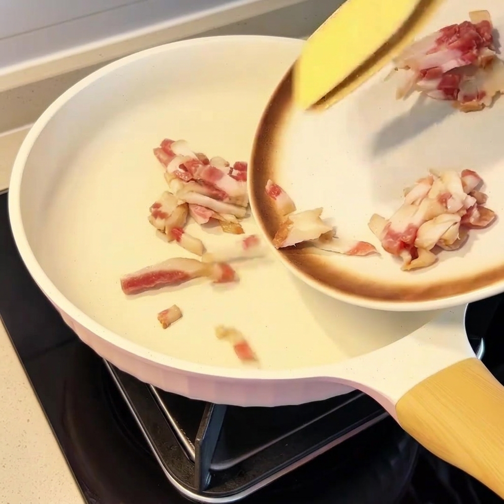 Trozos de guanciale distribuidos uniformemente en una sartén fría.