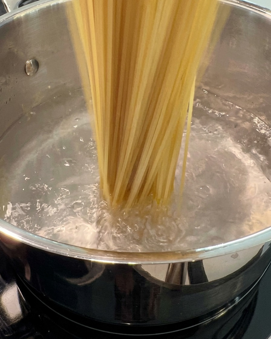 Fideos de espagueti secos sumergiéndose en una olla grande con agua hirviendo.