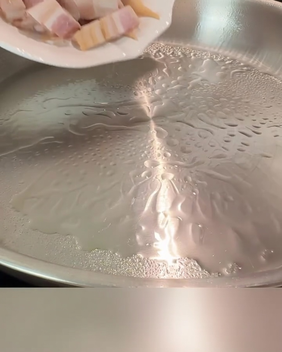 Trozos de tocino chisporroteando en una sartén caliente hasta quedar dorados y crujientes.