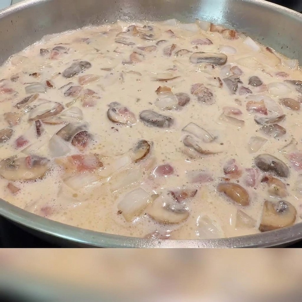 Sal y pimienta negra siendo espolvoreadas en la salsa cremosa de tocino y champiñones.