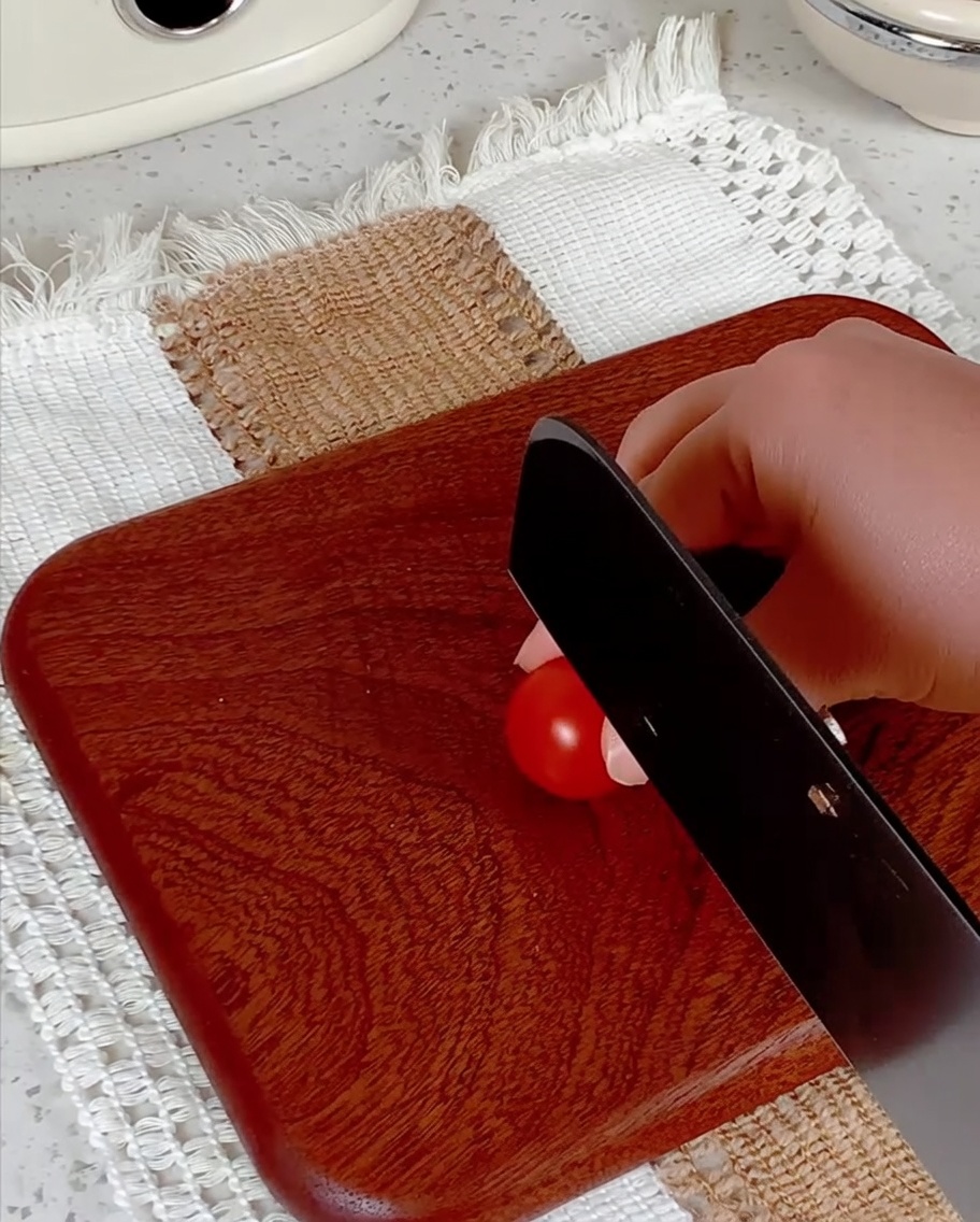 Tomates cherry siendo cortados a la mitad sobre una tabla de madera.